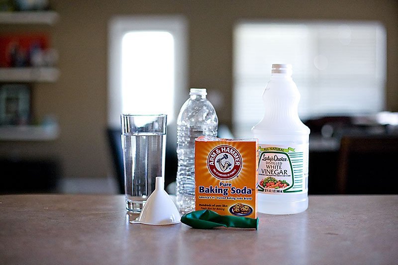 A glass of water, a funnel, an empty plastic bottle, an un-inflated balloon, a packet of baking soda and a bottle of white vinegar.