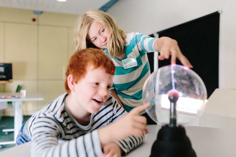 Children in a classroom experiment with toughing a 'Plasma globe' and observe how the bright filaments of static electric current are drawn to their touch.