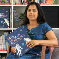 Dr Kanani sits in front of bookshelves holding her book