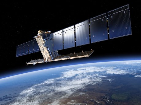 Artist's photo-realistic impression of the Sentinel-1 satellite viewed above the earth. The satellite is an inverted 'T' shape which is gold-plated, with two long arms of solar panels extending from either side of the main body.